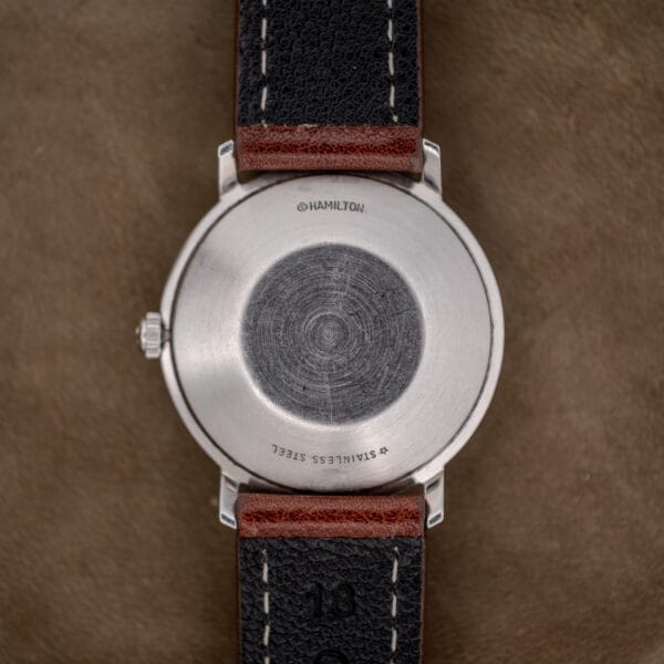 The Hamilton Automatic Silver Linen Dial Stainless Steel Cal. 689A, featuring a black and brown leather strap, rests on a brown surface, highlighting its refined style.