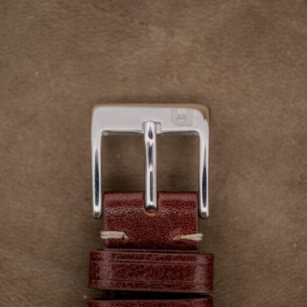 Close-up of a brown leather strap with a silver buckle, perfectly complementing the Hamilton Automatic Silver Linen Dial Stainless Steel Cal. 689A on a textured brown surface.