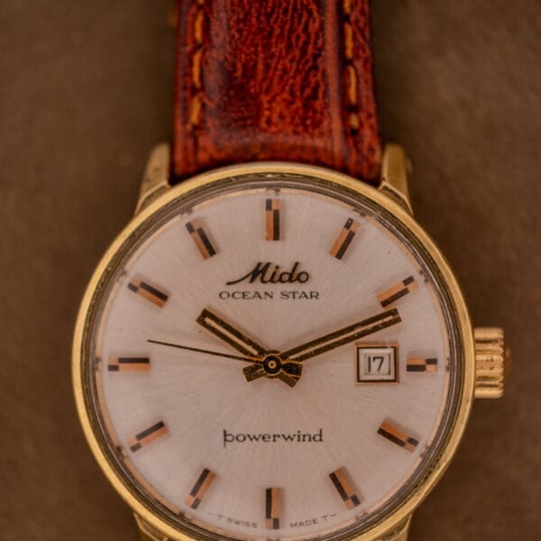 A Mido Ocean Star Powerwind Date Ladies Gold Tone wristwatch with an elegant gold tone case and brown leather strap.