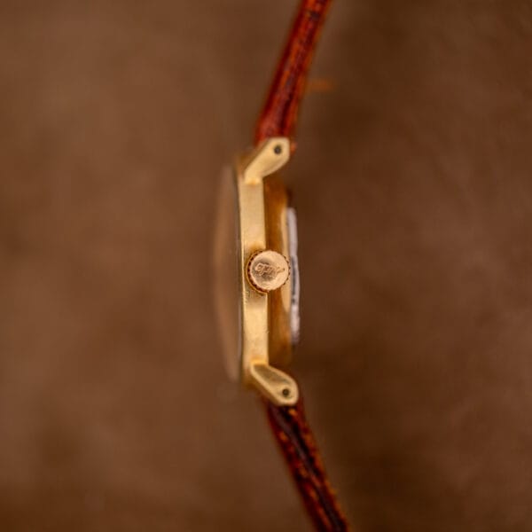 Close-up side view of the Mido Ocean Star Powerwind Date Ladies Gold Tone wristwatch with a brown leather strap, set against a warm brown background.