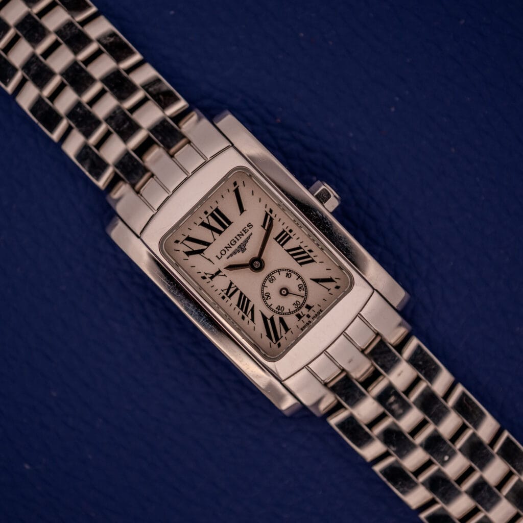 The Longines Dolce Vita L5.155.4 wristwatch features a rectangular stainless steel tank case and band, displayed on a dark blue background.