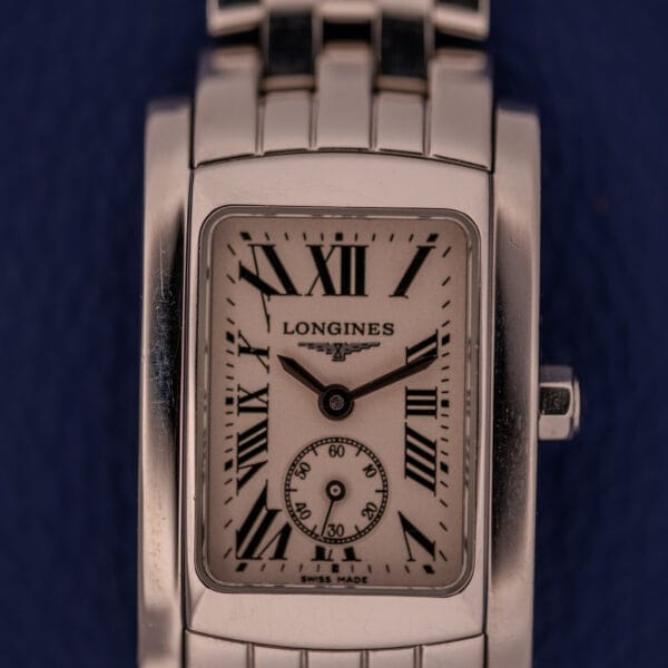 The Longines Dolce Vita L5.155.4 wristwatch features a stainless steel tank case, Roman numerals, and a small seconds subdial, showcased against a dark blue background.