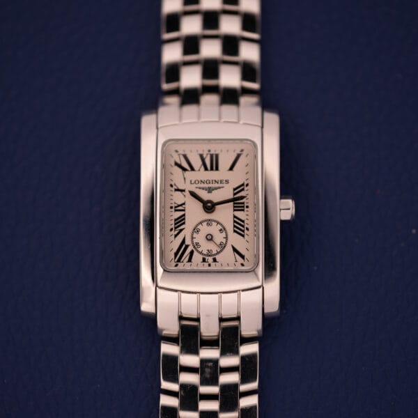 The Longines Dolce Vita L5.155.4 features a stainless steel Tank case, Roman numerals, and a linked band, showcased against a dark blue background.