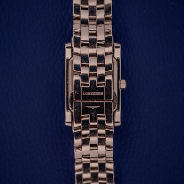 The Longines Dolce Vita L5.155.4 wristwatch, featuring a stainless steel tank case and link band, is displayed against a dark blue textured background.