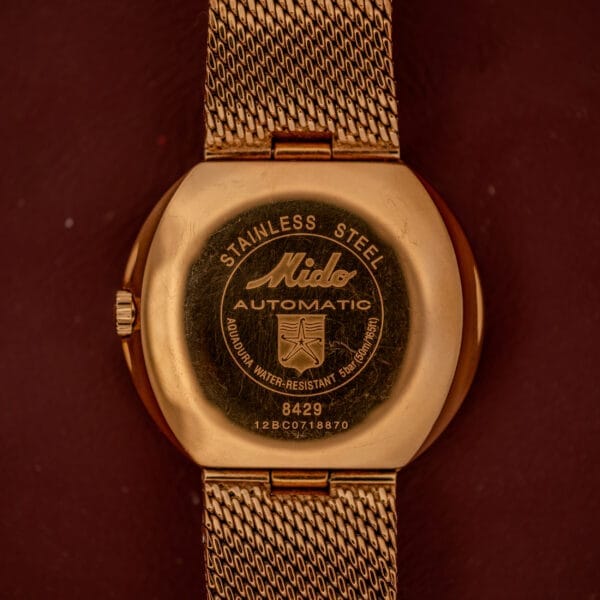 The Mido Commander Automatic Datoday Ref. 8429 features a gold case back with a Milanese strap, engraved with the brand name, model number, and water resistance details.