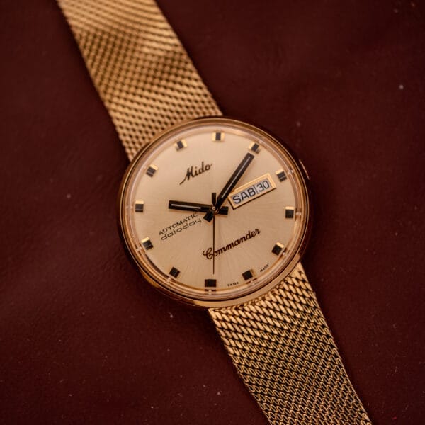 Mido Commander Automatic Datoday Ref. 8429 with Milanese strap, displaying day and date, shown on a brown surface.