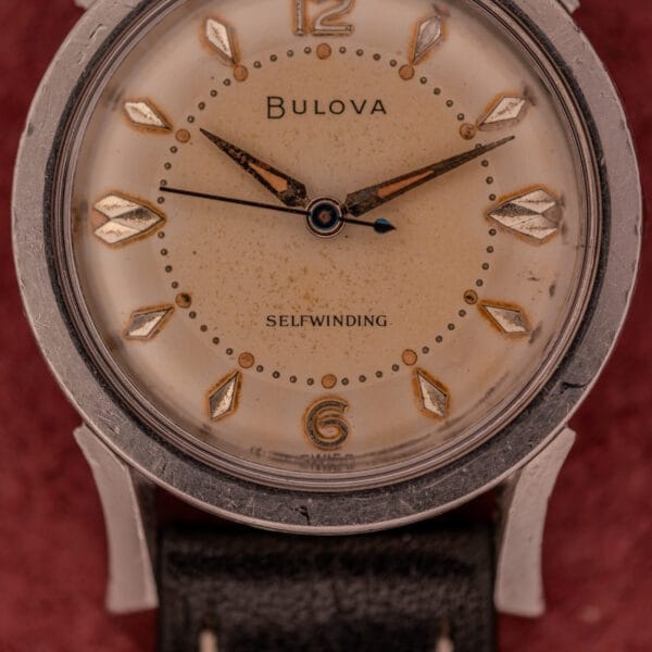 Close-up of a Bulova Self-Winding Cal. 11AFAC with a worn face, gold markers, black leather strap, and classic stainless steel case with fancy lugs.