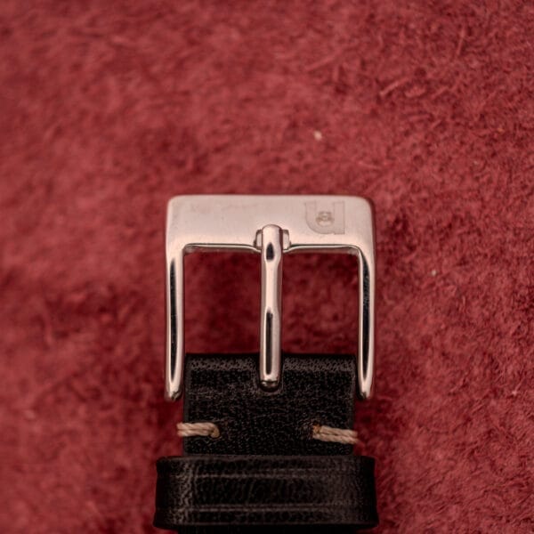 A silver buckle, echoing the Bulova Self-Winding Cal. 11AFAC Stainless Steel Case Fancy Lugs, is fastened to a black leather belt set against a textured red background.