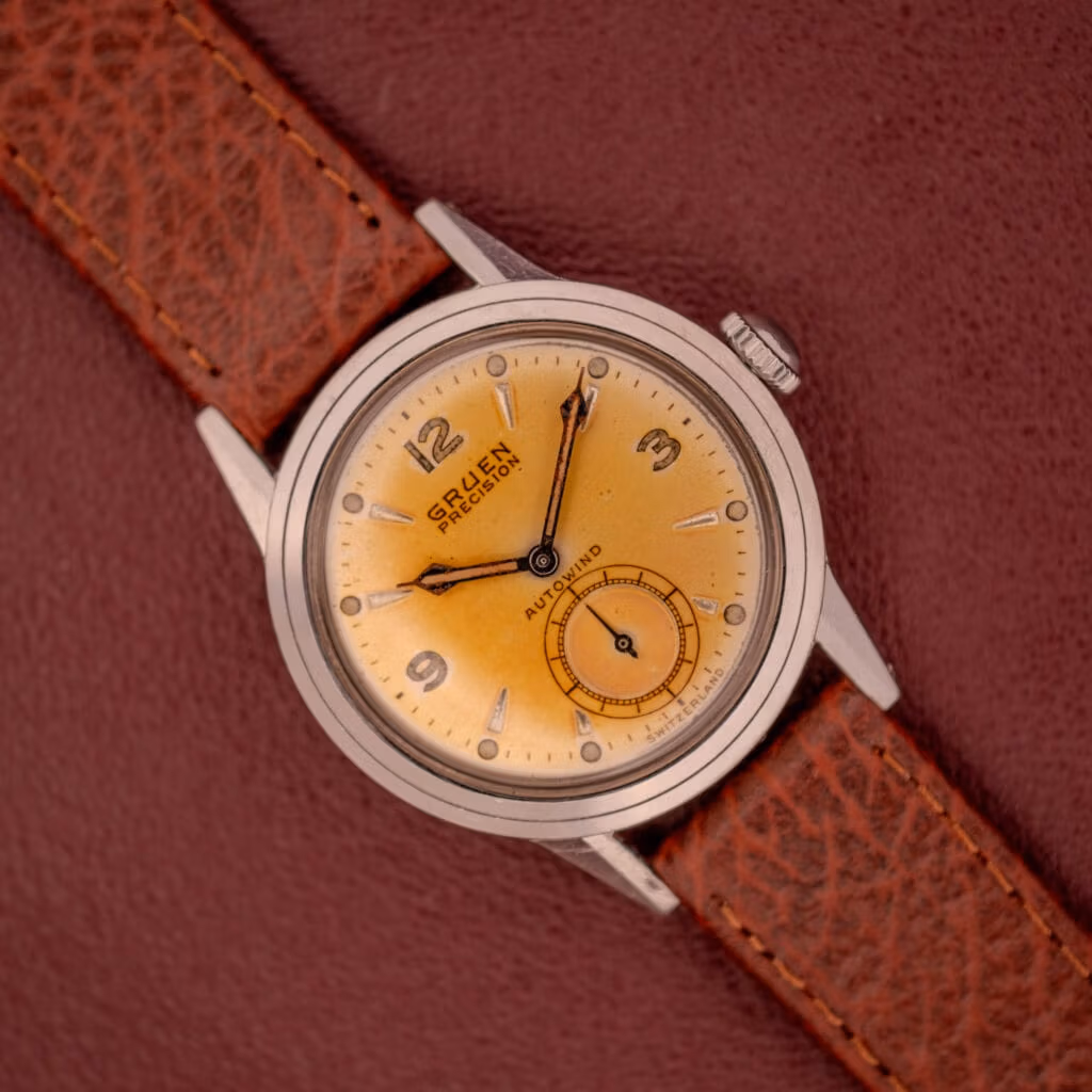 Gruen Precision Auto-Wind Cal. 400 wristwatch with a copper dial and stainless steel case, paired with a brown leather strap, displayed on a brown textured background.