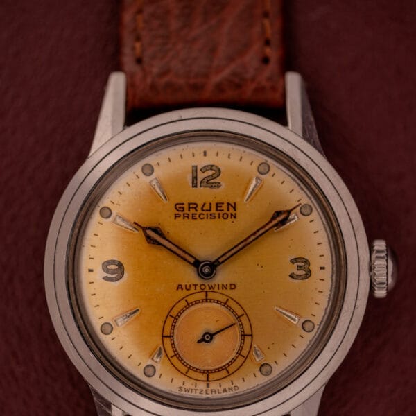 Gruen Precision Auto-Wind Copper Dial Stainless Steel Cal. 400 wristwatch with a brown leather strap on a maroon background.