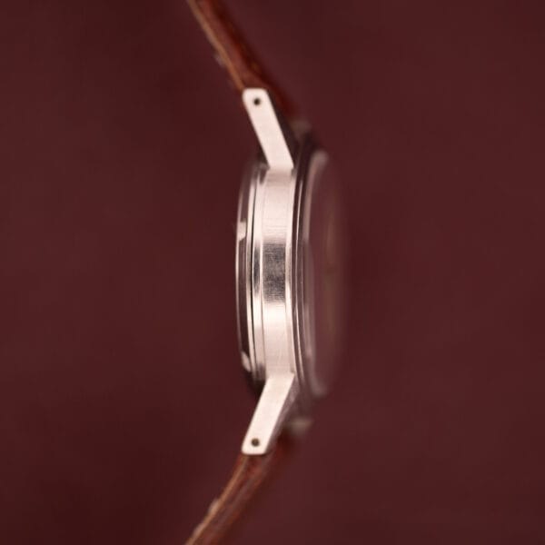 Side view of a Gruen Precision Auto-Wind Copper Dial Stainless Steel Cal. 400 wristwatch with a brown leather strap, set against a maroon background.