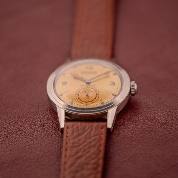 A Gruen Precision Auto-Wind with a copper dial and stainless steel Cal. 400 case is displayed on a textured brown surface, paired with a brown leather strap for a timeless vintage look.