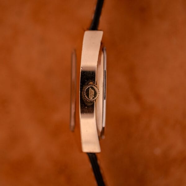 Side view of a Mido Automatic Multi Star Datoday Cal. 1819 Ref. 6929300 gold wristwatch with a black strap, set against a brown background.