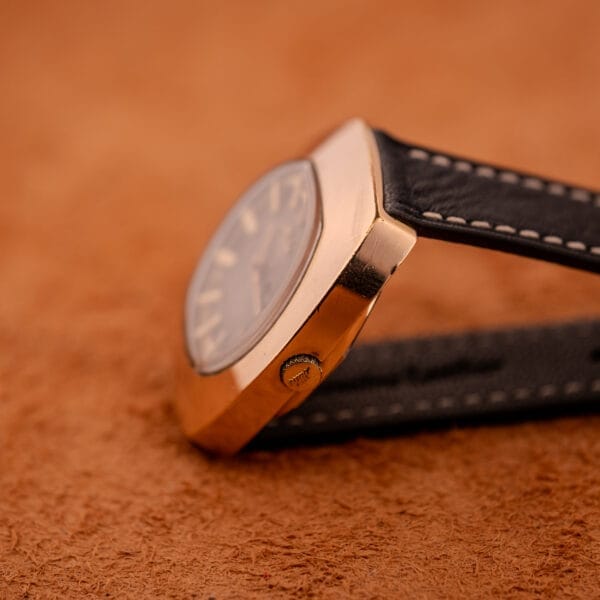 Close-up of a Mido Automatic Multi Star Datoday Cal. 1819 Ref. 6929300 wristwatch with a black leather strap and gold casing on a brown textured surface.