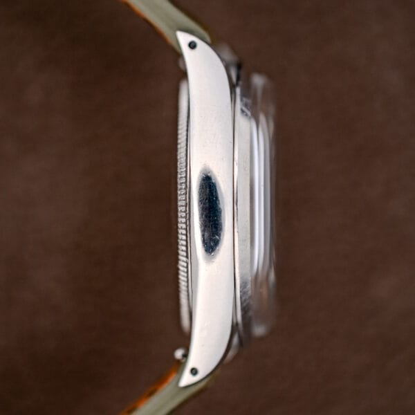 A close-up side view of a Rolex Oyster Perpetual Air King Ref. 5500 Silver Sunburst Dial wristwatch featuring a visible dark scratch on the metal case.