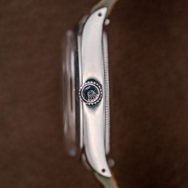 Side view of a Rolex Oyster Perpetual Air King Ref. 5500 with a silver sunburst dial, featuring the engraved crown and Rolex logo against a brown background.