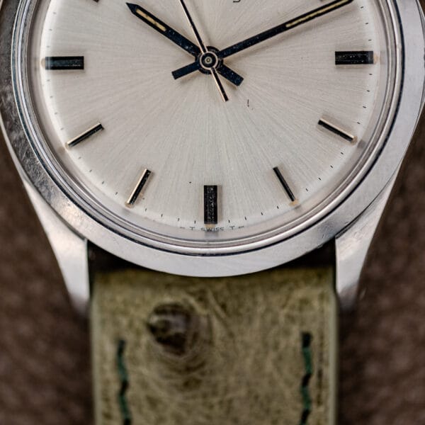 Close-up of a Rolex Oyster Perpetual Air King Ref. 5500 with a silver sunburst dial, black markers, and a green leather strap.