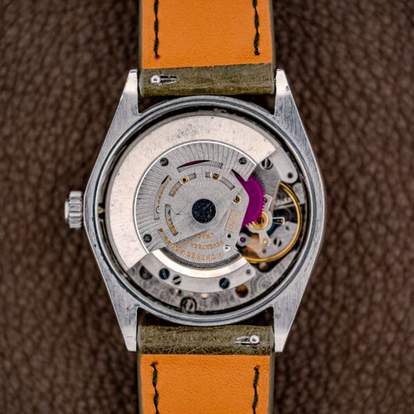 Close-up of a Rolex Oyster Perpetual Air King Ref. 5500 with a silver sunburst dial, paired with a brown leather strap and displayed on a textured brown surface.