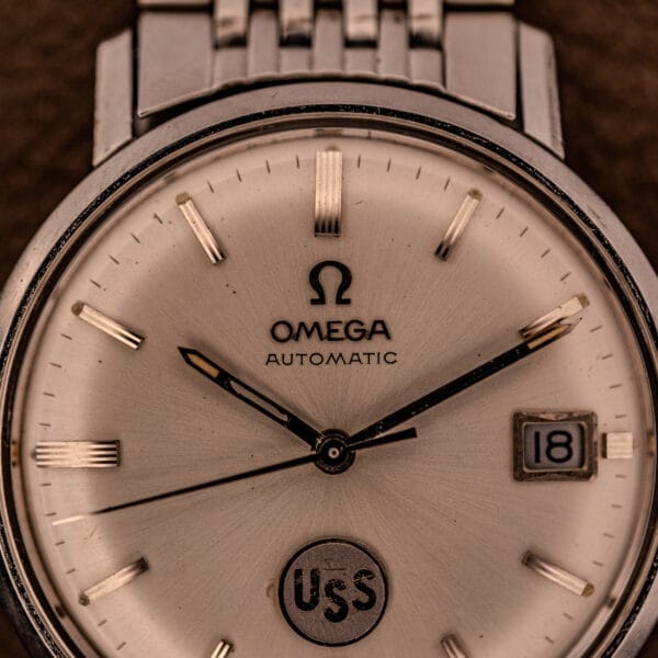 Close-up of an Omega Automatic Ref. 166.020 for U.S. Steel Presentation Watch, featuring a metal band, date display, and USS inscription on the dial.