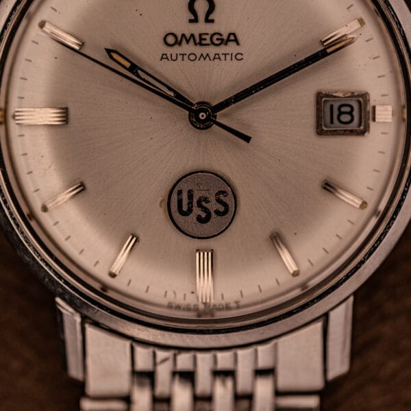 Close-up of the Omega Automatic Ref. 166.020 for U.S. Steel Presentation Watch, showing "USS" on the dial and the date set to 18—a classic timepiece awarded by U.S. Steel.