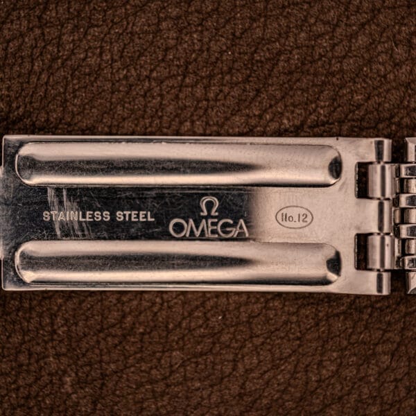 Close-up of an Omega Automatic Ref. 166.020 for U.S. Steel Presentation Watch clasp, shown resting on a brown textured surface.