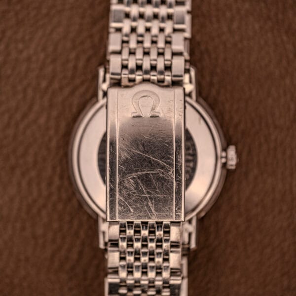 Silver Omega Automatic Ref. 166.020 clasp with visible scratches, pictured on a brown textured background; from a U.S. Steel Presentation Watch.
