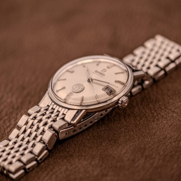 An Omega Automatic Ref. 166.020 for U.S. Steel Presentation Watch with a metal band rests on a brown textured surface.