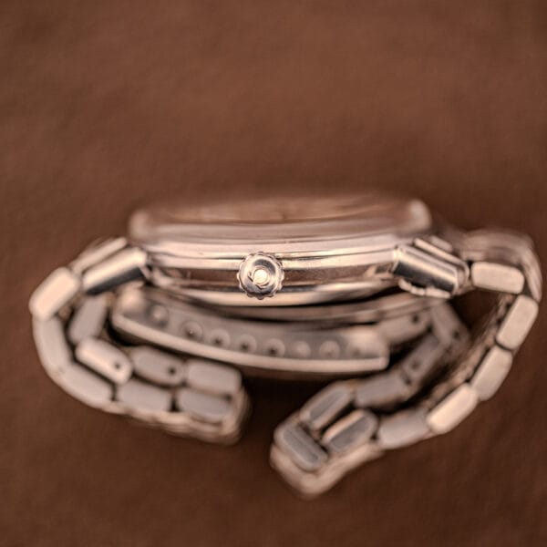 Close-up of the Omega Automatic Ref. 166.020 for U.S. Steel Presentation Watch, silver with a metal band, displayed on its side against a brown background.