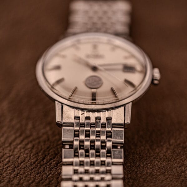 Close-up of an Omega Automatic Ref. 166.020 for U.S. Steel Presentation Watch with a metal band, elegantly displayed on a brown textured surface.