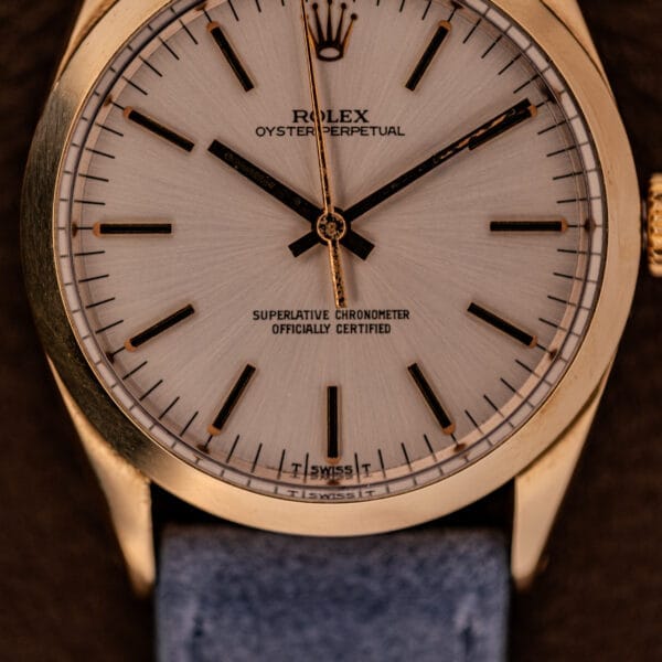 Close-up of a Rolex Oyster Perpetual 1024 14k Gold Capped watch featuring a sunburst dial, black hour markers, and a blue strap.