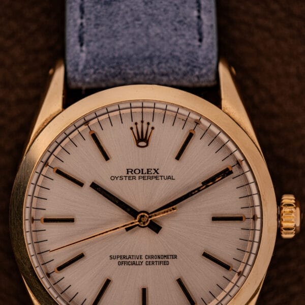 Close-up of a Rolex Oyster Perpetual 1024, capped in 14k gold with a sunburst dial and paired with a blue leather strap.