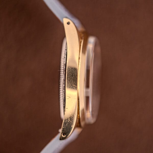 Side view of a Rolex Oyster Perpetual 1024 14k Gold Capped wristwatch with sunburst dial and white strap, set against a brown background.