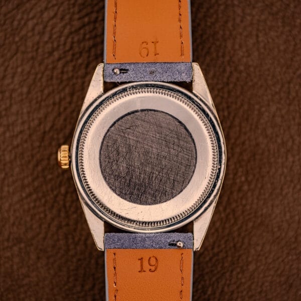 A scratched Rolex Oyster Perpetual 1024 14k Gold Capped with a tan leather strap rests on a brown textured surface, highlighting its elegant sunburst dial.