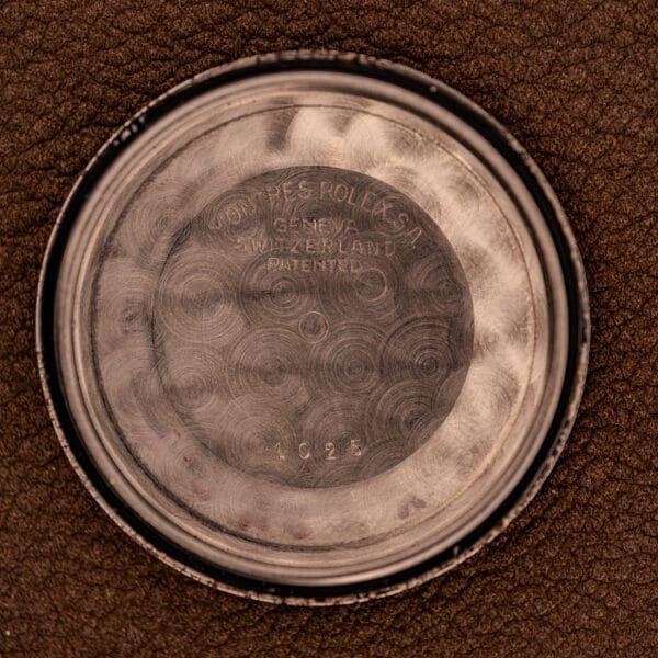 Close-up of a Rolex Oyster Perpetual 1024 14k Gold Capped & Sunburst Dial watch case back with engraved text and numbers, set against a brown textured background.