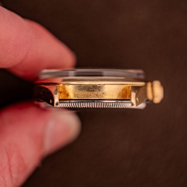 Close-up of fingers holding a Rolex Oyster Perpetual 1024 14k Gold Capped & Sunburst Dial wristwatch, focusing on the engraved serial number on its side.
