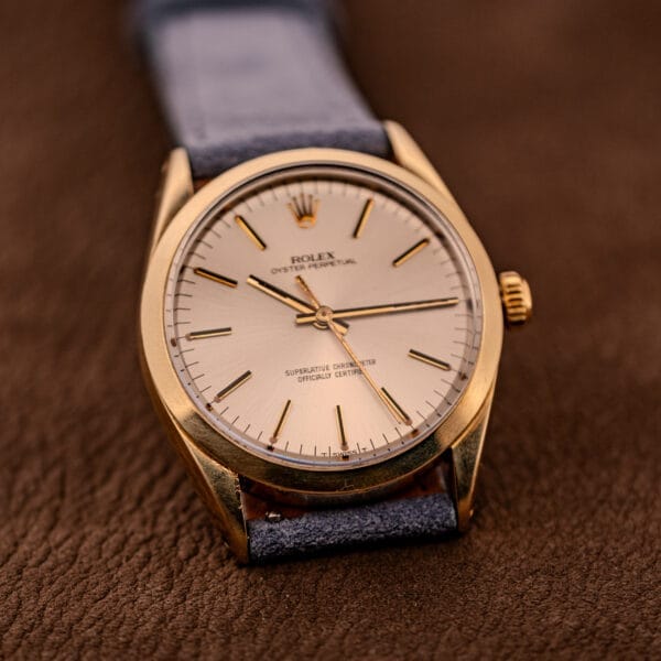 A Rolex Oyster Perpetual 1024 14k Gold Capped with a sunburst dial and leather strap rests on a brown textured surface.
