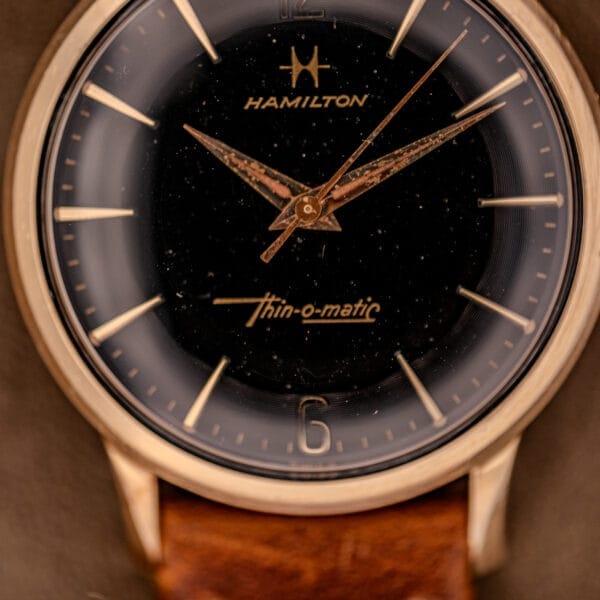 Close-up of a Hamilton Thin-O-Matic Black Dial 10k Gold Filled Case Cal. 663 wristwatch with a brown leather strap and vintage appeal.