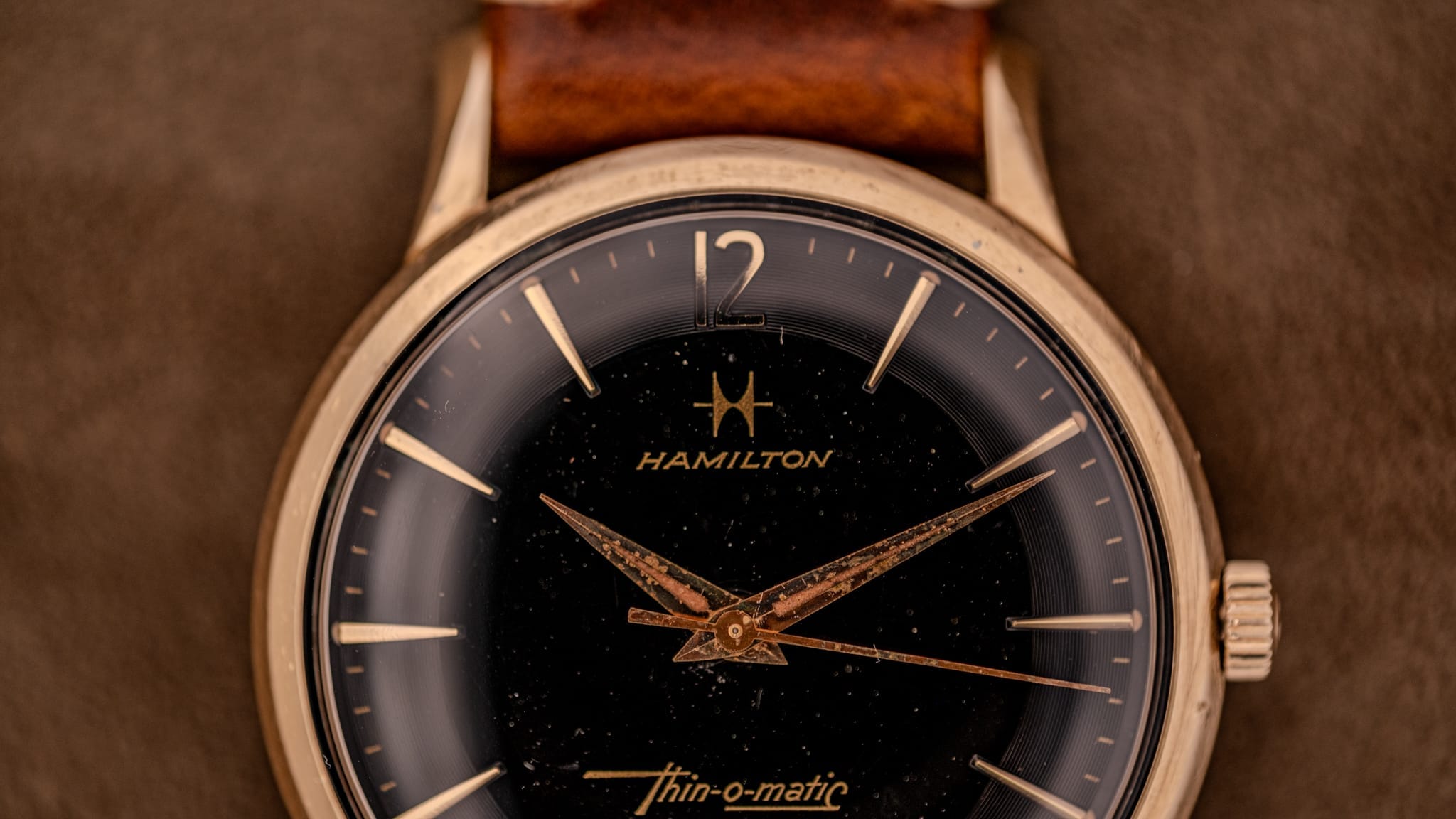 Close-up of a vintage Hamilton Thin-o-matic wristwatch, featuring a brown leather strap and elegant gold details.