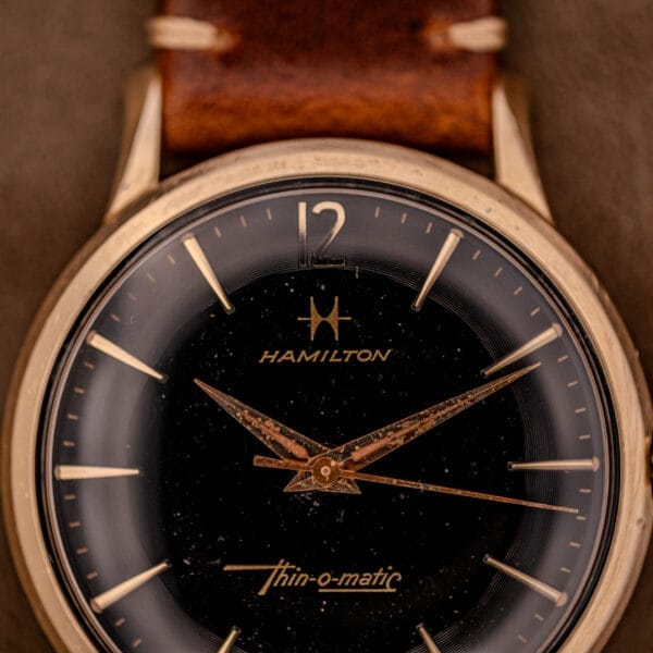Close-up of a Hamilton Thin-O-Matic Black Dial 10k Gold Filled Case Cal. 663 wristwatch, featuring a brown leather strap and elegant gold detailing.