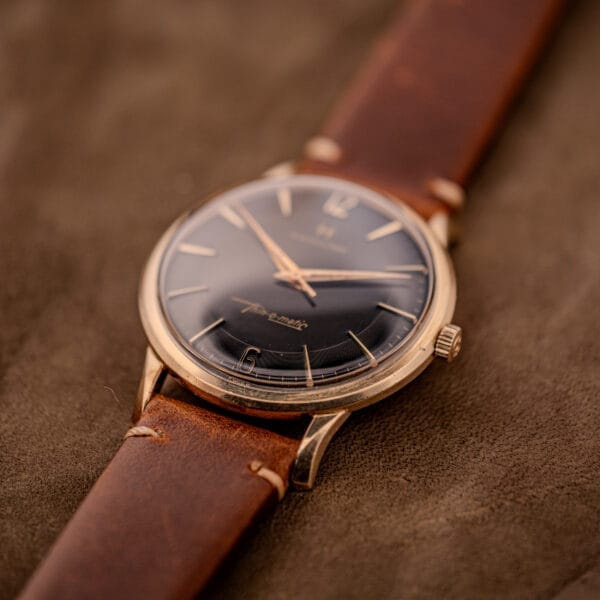 A Hamilton Thin-O-Matic Black Dial 10k Gold Filled Case Cal. 663 wristwatch with a brown leather strap rests elegantly on a brown suede surface.