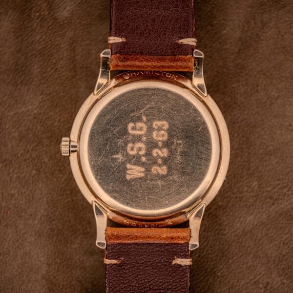A Hamilton Thin-O-Matic Black Dial wristwatch with a 10k gold filled case Cal. 663, engraved W.S.G. 2-2-63, and set on a brown leather strap is displayed elegantly on suede.