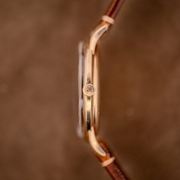 Side view of a Hamilton Thin-O-Matic Black Dial wristwatch with a 10k gold filled case, brown leather strap, and Cal. 663 movement, focusing on the crown against a brown background.