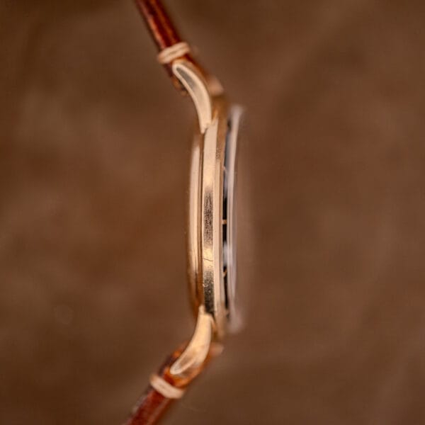 Side view of a Hamilton Thin-O-Matic Black Dial wristwatch, featuring a 10k Gold Filled Case (Cal. 663) and a brown leather strap, set against a brown background.