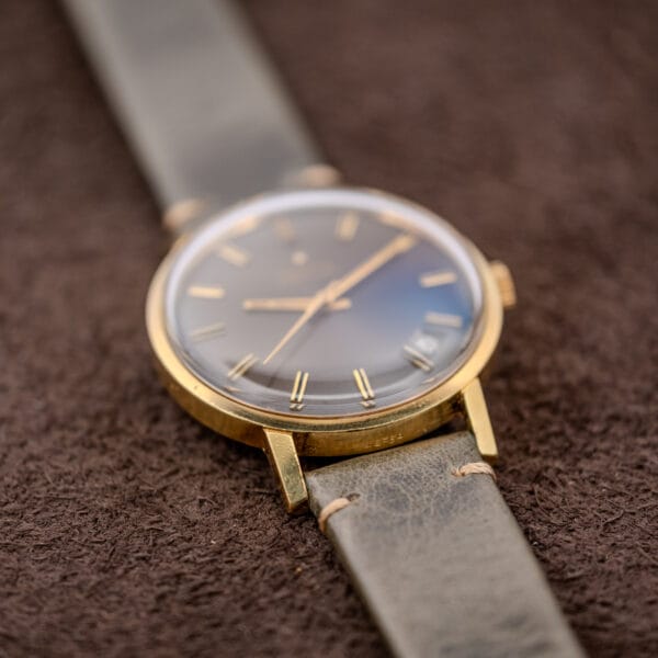 The Zenith Automatic Date Charcoal Sunburst Dial Cal. 2542 PC wristwatch with a leather strap is elegantly displayed on a textured brown surface.