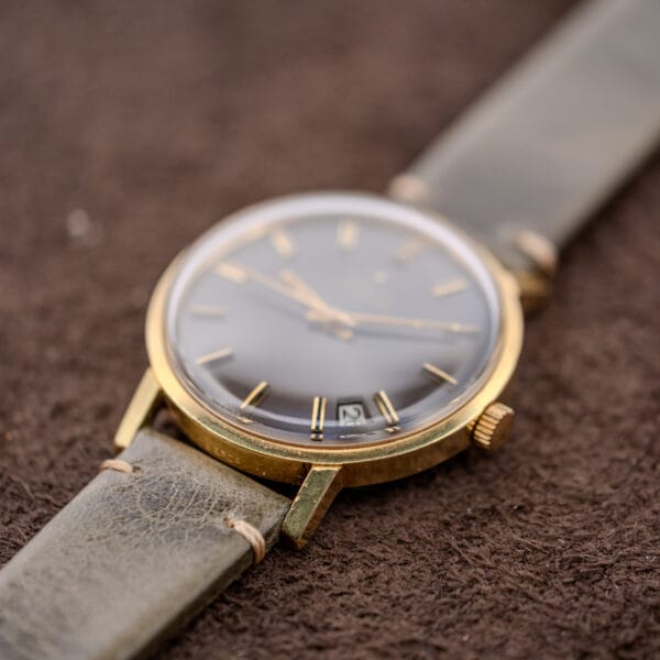 The Zenith Automatic Date features a Charcoal Sunburst Dial, Cal. 2542 PC movement, and leather strap—shown here resting on a brown textured surface.