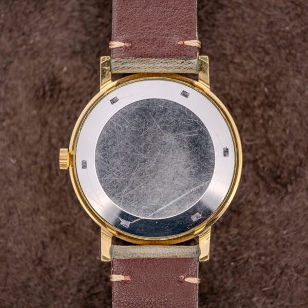 A Zenith Automatic Date Charcoal Sunburst Dial Cal. 2542 PC wristwatch with a brown leather strap rests on a brown textured surface, showcasing its refined style and subtle automatic date feature.