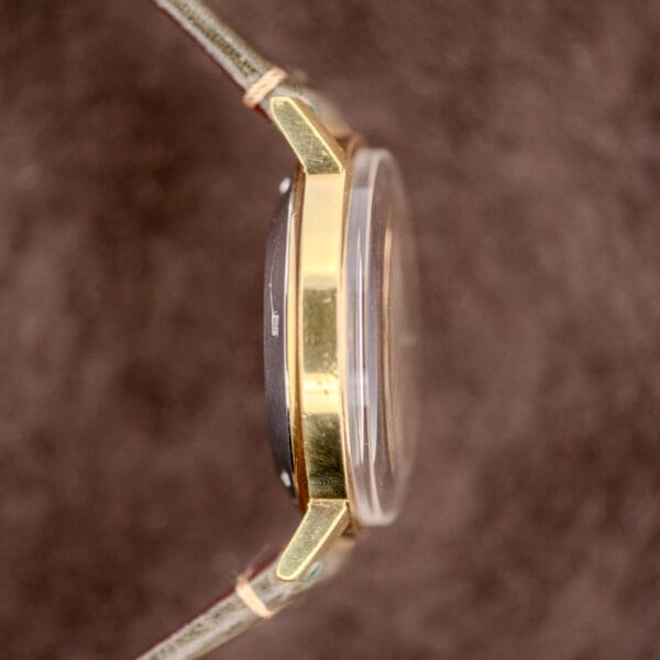 Side view of the Zenith Automatic Date Charcoal Sunburst Dial Cal. 2542 PC wristwatch with a charcoal sunburst dial, domed crystal, and green fabric strap shown on a brown background.