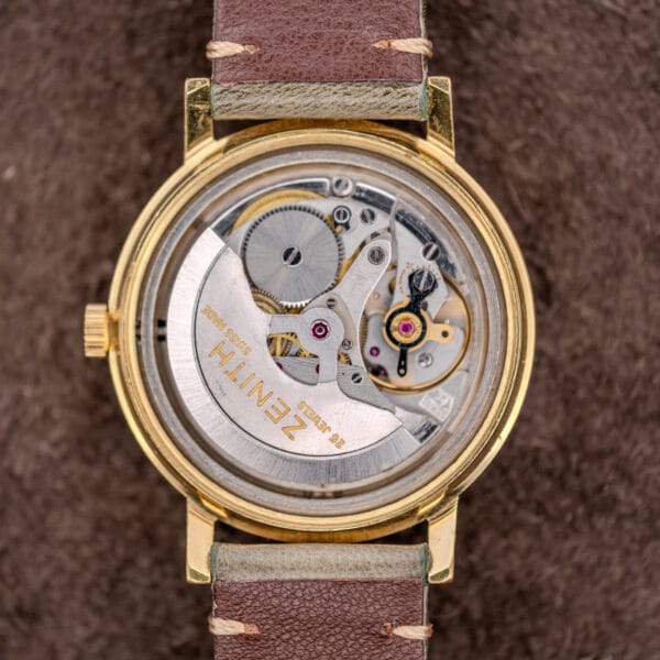 Close-up of Zenith Automatic Date Charcoal Sunburst Dial Cal. 2542 PC with exposed mechanical movement, gold case, and brown leather strap.