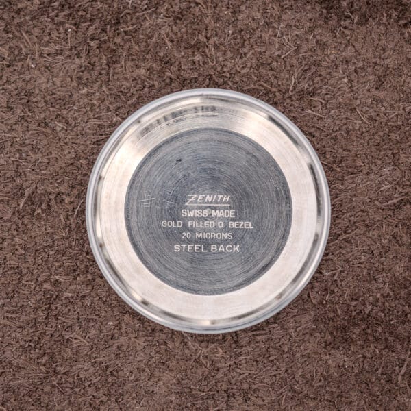 The Zenith Automatic Date Charcoal Sunburst Dial Cal. 2542 PC features an engraved case back on a brown textured surface, reflecting elegance and showcasing its renowned Cal. 2542 movement.