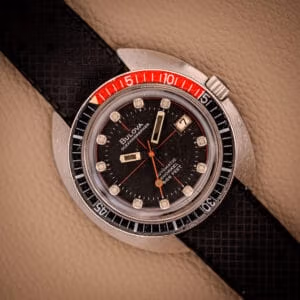 A vintage Bulova Oceanographer Automatic Snorkel 714 Red Cross Hair Dial watch featuring a black dial, red and black bezel, and a textured black strap.
